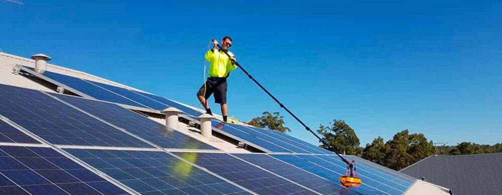 Green Sun Solutions team member cleaning solar panels on a roof