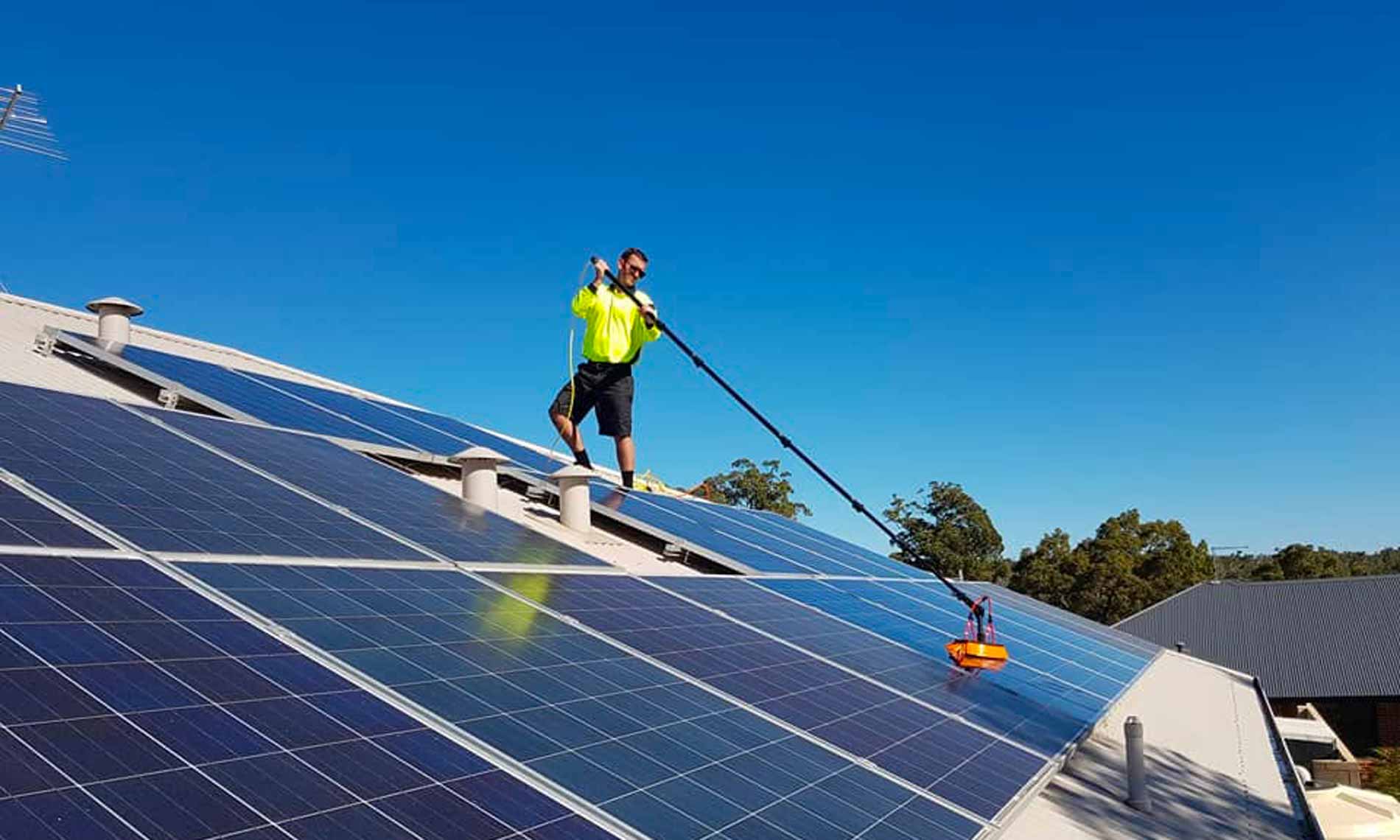 Green Sun Solutions team member cleaning solar panels on a roof